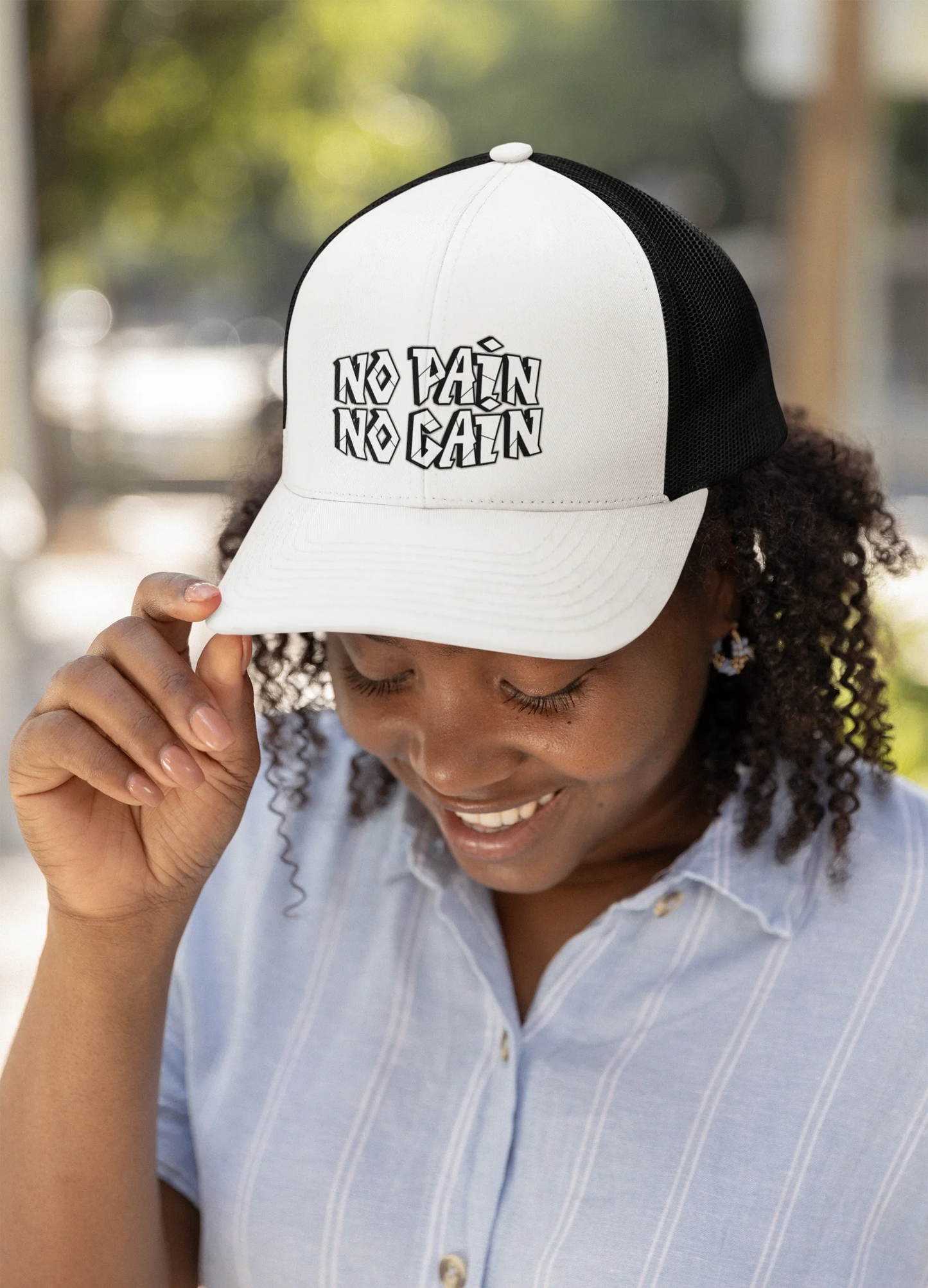 Woman in casual shirt wearing MY$TOAR trucker hat with 'No Pain No Gain' print outdoors