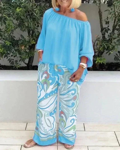 Woman wearing light blue off-shoulder top and floral print pants, MY$TOAR luxury apparel